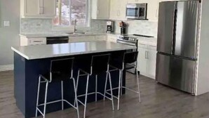 A modern kitchen with white cabinets, a stainless steel refrigerator, and a central island with bar stools.