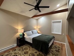 A bedroom with a bed, two bedside lamps, a ceiling fan, a window with blinds, and a patterned carpet.