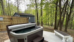 A hot tub with a wooden deck, a bench, and a wooden fence in a wooded area. - Secluded cozy cabin with modern amenities/hot tub/pet friendly/wifi (Berkeley Springs)