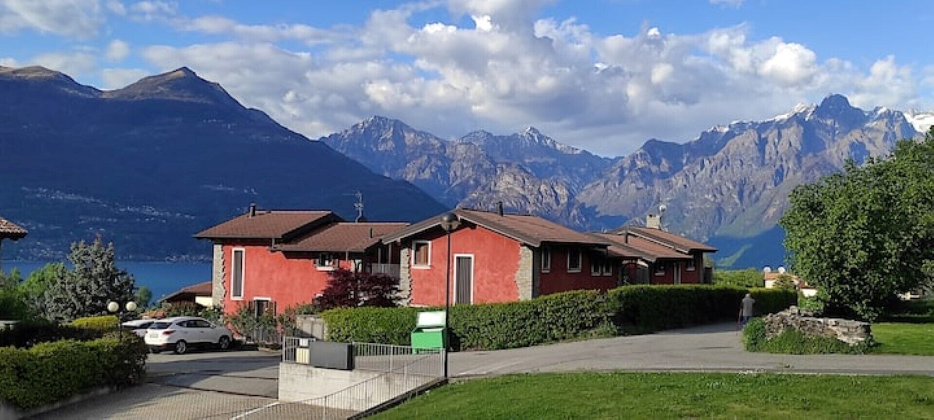 A red building with a sloped roof, a paved driveway, and a view of mountains in the background.