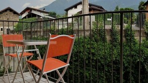 Una terraza con una mesa y sillas, una cerca de metal y vistas a montañas al fondo.