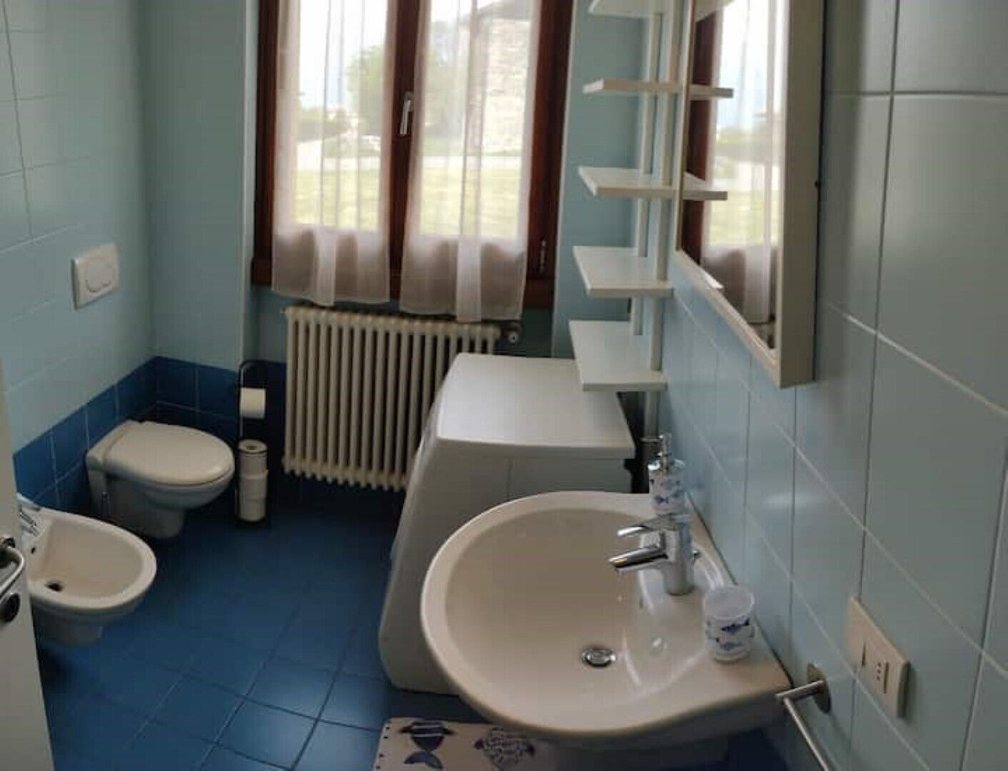 Een kleine badkamer met toilet, bidet, wastafel en spiegel.