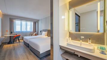 Habitación de hotel con cama, escritorio, silla, espejo grande y baño con lavabo y espejo.