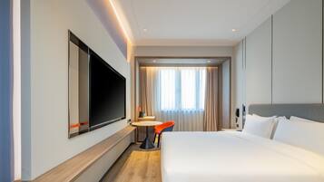 A hotel room with a large bed, a flat-screen TV mounted on the wall, a small round table, and a chair.