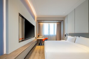 A hotel room with a large bed, a flat-screen TV mounted on the wall, a small round table, and a chair.