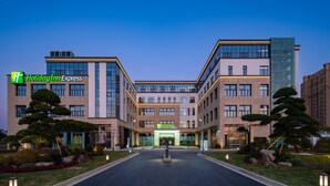 Un hotel Holiday Inn Express con un diseño arquitectónico moderno, que presenta una entrada central, jardines ajardinados y una fachada bien iluminada.