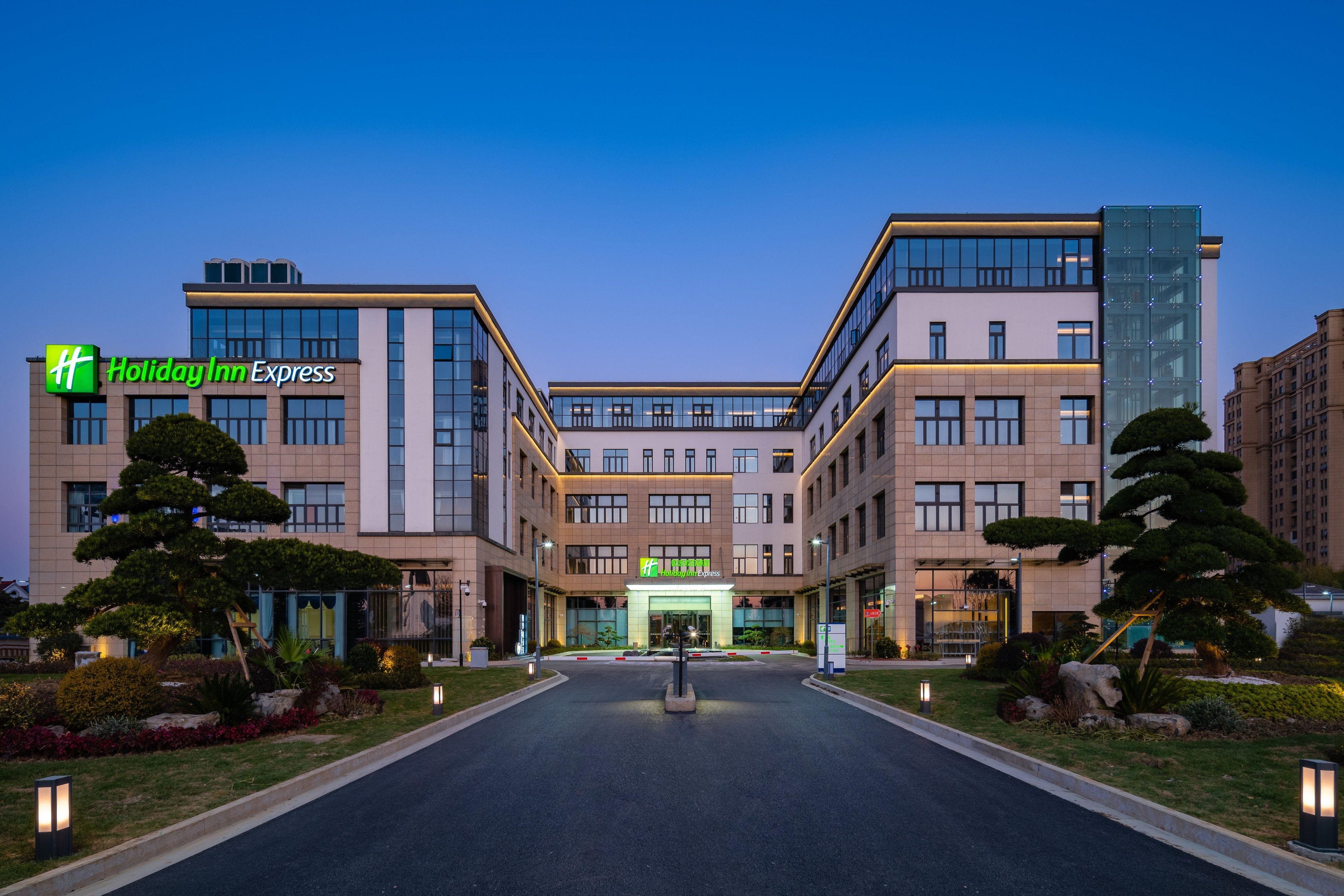 Een Holiday Inn Express hotel met een modern architecturaal ontwerp, met een centrale ingang, aangelegde tuinen en een goed verlichte gevel.