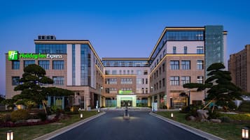 Een Holiday Inn Express hotel met een modern architecturaal ontwerp, met een centrale ingang, aangelegde tuinen en een goed verlichte gevel.