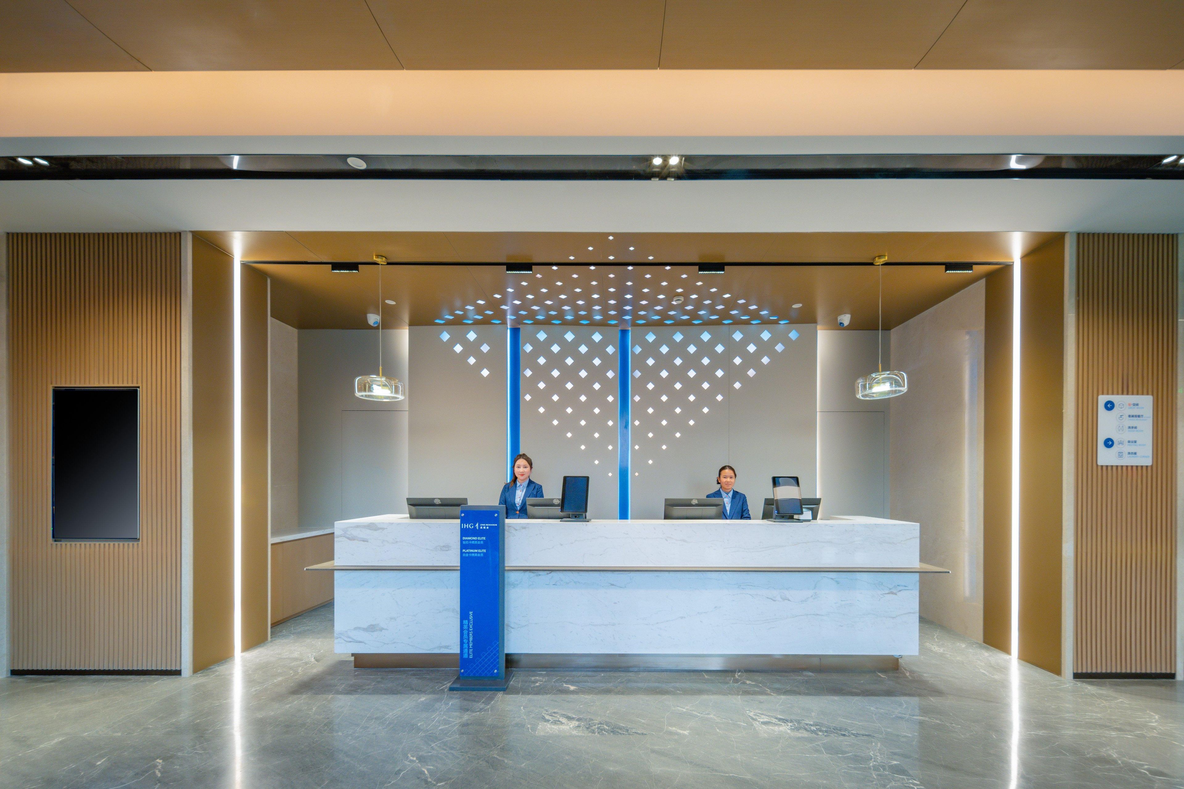 A reception desk with two staff members, a blue sign, and a patterned wall design.