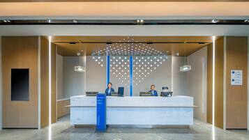 A reception desk with two staff members, a blue sign, and a patterned wall design.
