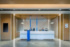 A reception desk with two staff members, a blue sign, and a patterned wall design. - Holiday Inn Express Suzhou Luzhi (Suzhou)