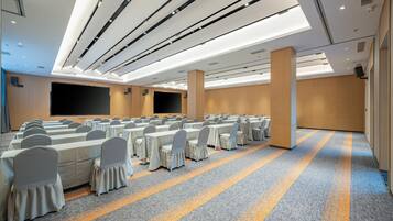 Un salón de conferencias con mesas y sillas dispuestas en filas, una pantalla grande y suelo alfombrado.
