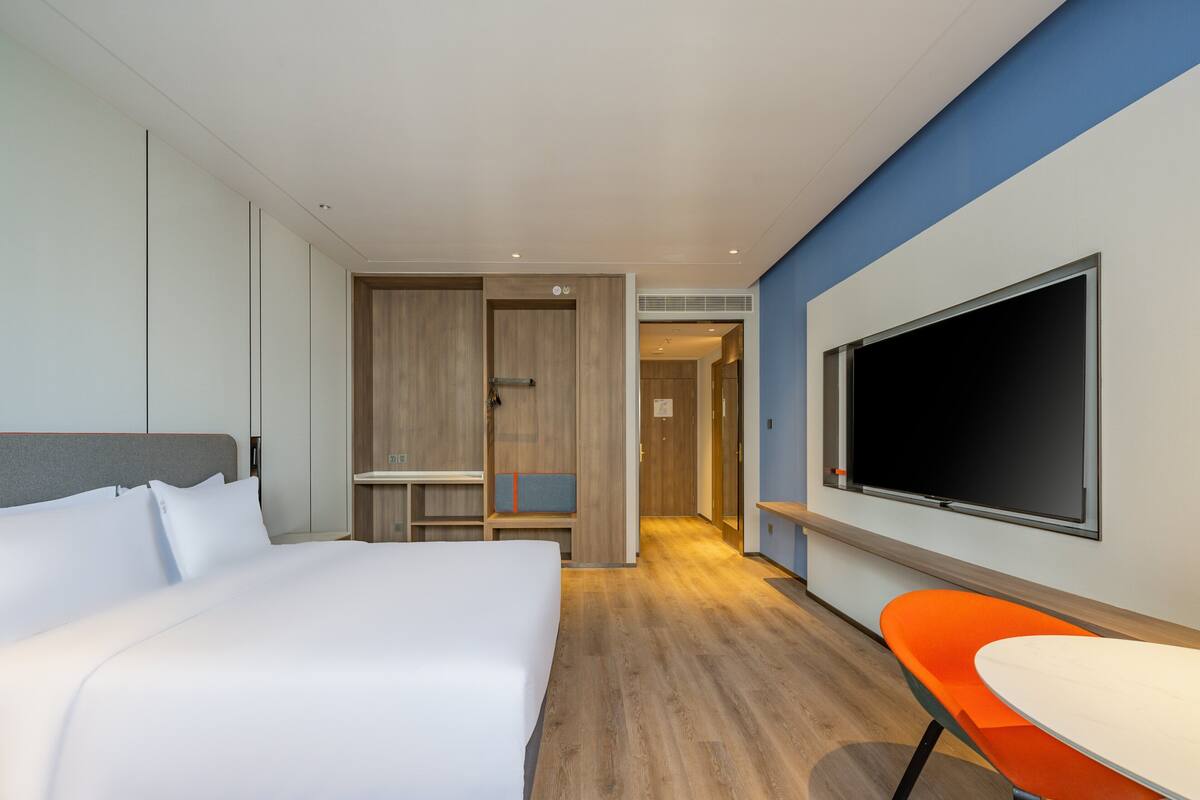 Quarto de hotel com cama, televisão, escrivaninha e uma cadeira.