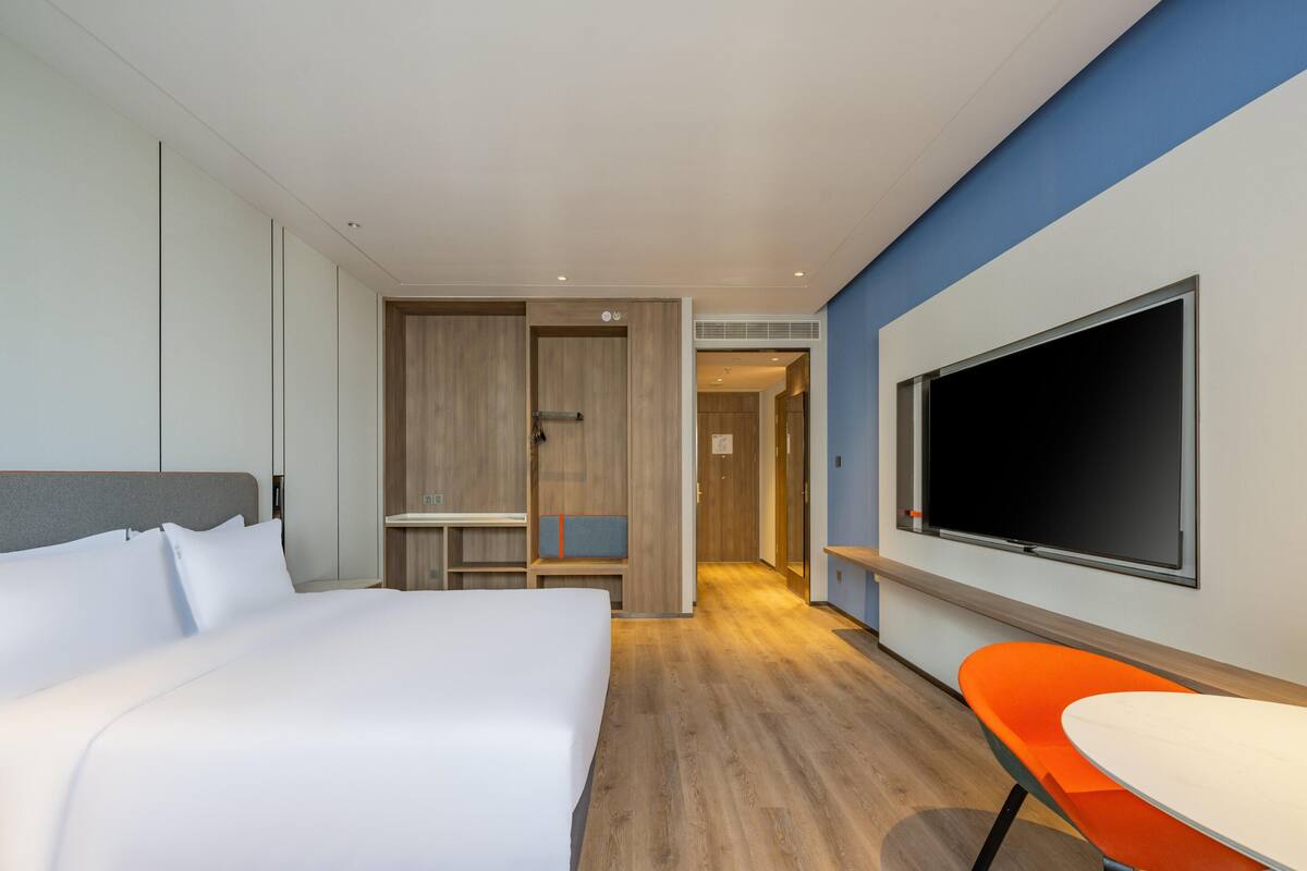 Quarto de hotel moderno com uma cama grande, uma televisão, uma escrivaninha e uma cadeira.