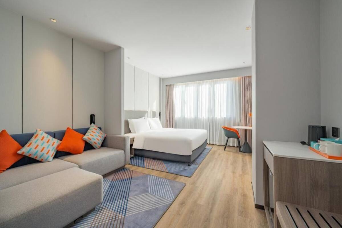 Quarto de hotel com cama, escrivaninha, poltrona, sofá e pequena mesa com cafeteira.