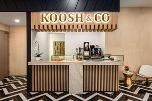 A reception area with a wooden sign reading "KOOSH & CO", a glass counter with various items, a potted plant, and a chair. - Dolce BY Wyndham Hollywood (HOLLYWOOD)