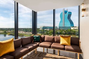A modern interior with a sectional sofa and large windows offering a view of a unique building and a body of water. - Dolce BY Wyndham Hollywood (HOLLYWOOD)
