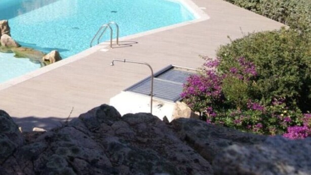 Une piscine agrémentée d’une formation rocheuse, d’une petite terrasse et d’une échelle en métal.
