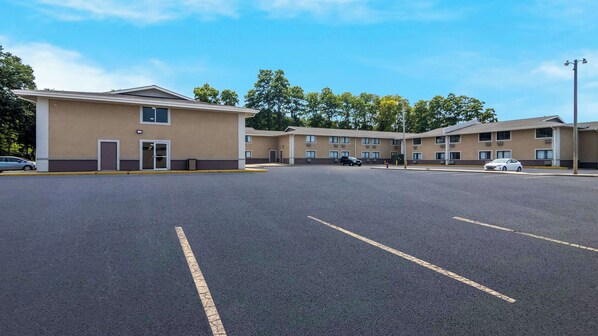 A parking lot with a row of single-story buildings, each with a door and windows, and a clear sky above.