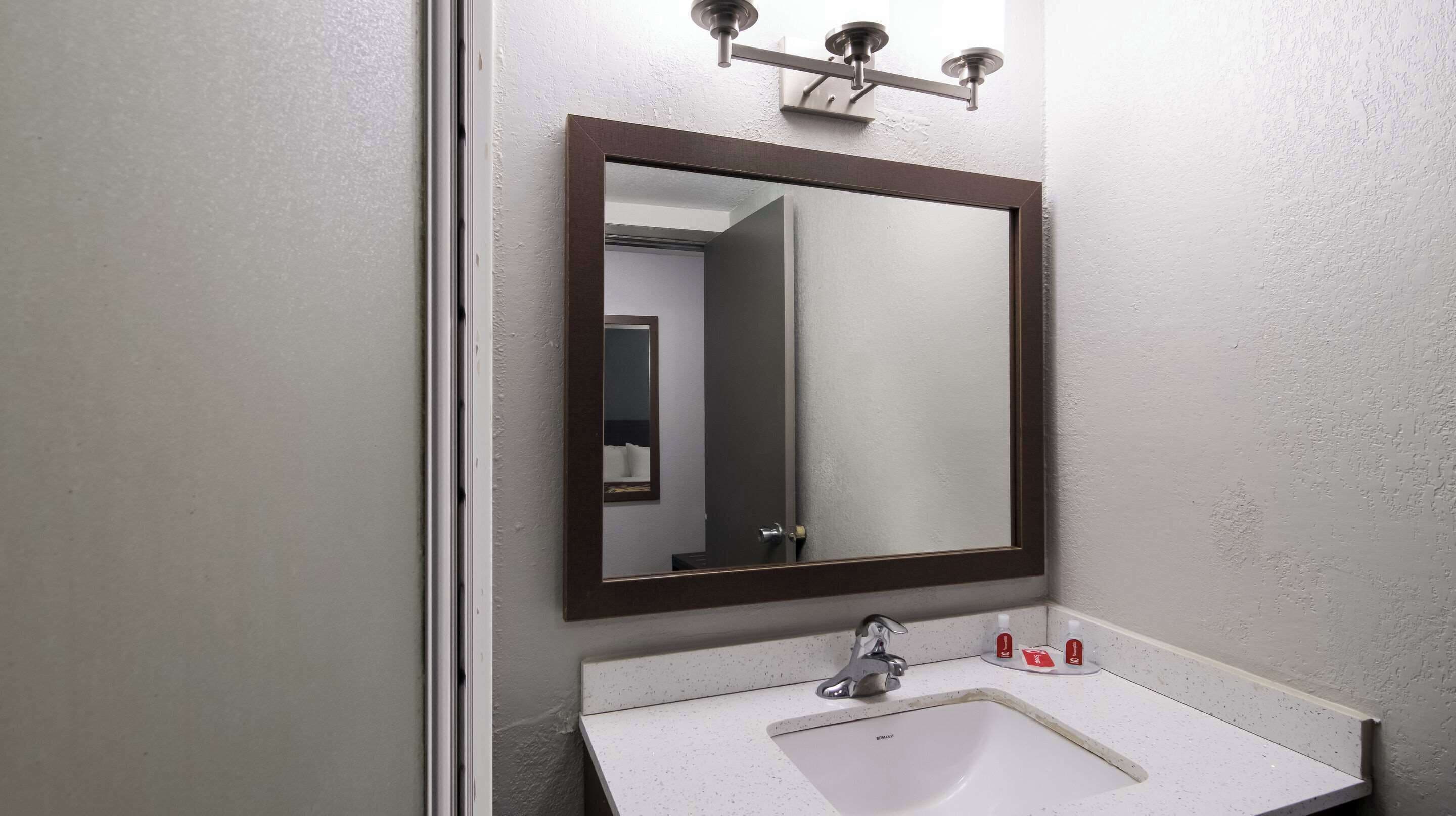 A bathroom with a white sink, a mirror, and a light fixture above the mirror.