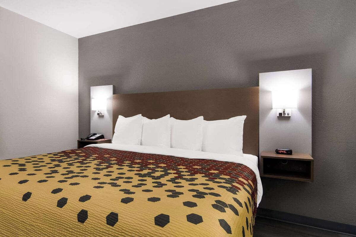 A hotel room with a large bed, a patterned bedspread, a nightstand with a telephone, and wall-mounted lights.