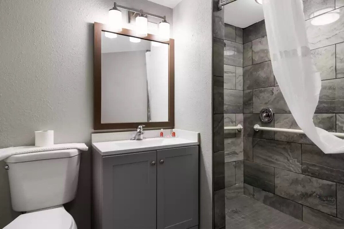 A bathroom with a toilet, sink, mirror, and shower with a curtain.