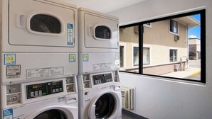 A laundromat with stacked washers and dryers, a window view of a building, and a sign indicating payment with a phone. - Econo Lodge Portage (Portage)