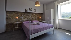 A bedroom with a stone wall, a bed with a metal frame, two bedside tables with lamps, and a wardrobe. - App.to Jasmine, sea view 450 meters, with equipped garden. (Castellabate, fraz. Ogliastro Marina)