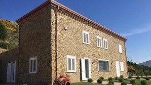 A stone building with a symmetrical facade, multiple windows with shutters, and a well-maintained garden with various shrubs and a decorative barrel. - App.to Jasmine, sea view 450 meters, with equipped garden. (Castellabate, fraz. Ogliastro Marina)