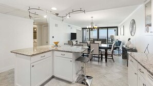 A modern kitchen with a granite countertop, white cabinetry, and a dining area with a table and chairs.