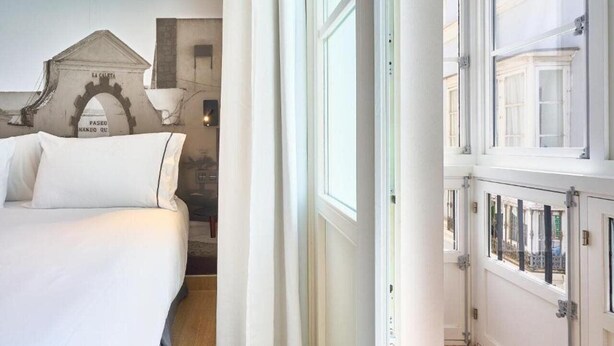 A hotel room with a bed, a window, and a view of the street. - Tandem Populo (Cádiz)