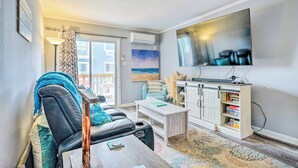 A living room with a sofa, coffee table, TV, and bookshelf. - North Topsail Condo - Steps to Beach! (North Topsail Beach)