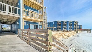 A multi-story building with balconies, a wooden deck, and a sandy beach in the background. - North Topsail Condo - Steps to Beach! (North Topsail Beach)