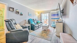 A living room with a leather sofa, a coffee table, and a TV mounted on the wall. There is a window with a view of the ocean. - North Topsail Condo - Steps to Beach! (North Topsail Beach)