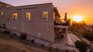 Un bâtiment à deux étages doté d’un balcon, d’un patio aménagé avec du mobilier d’extérieur et offrant une vue sur le coucher du soleil.