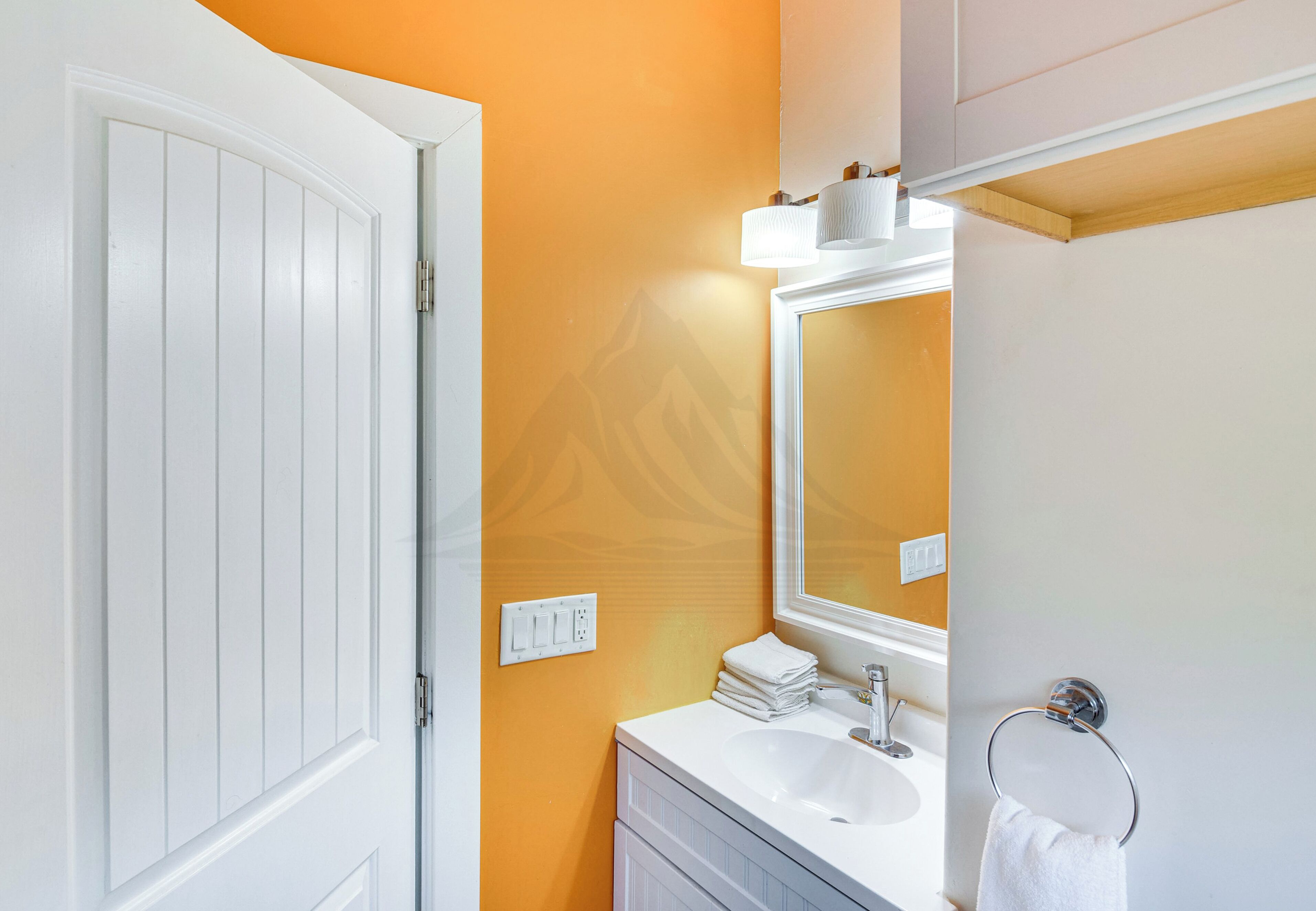 Une salle de bain avec un meuble-lavabo blanc, un évier, un miroir et un porte-serviettes.