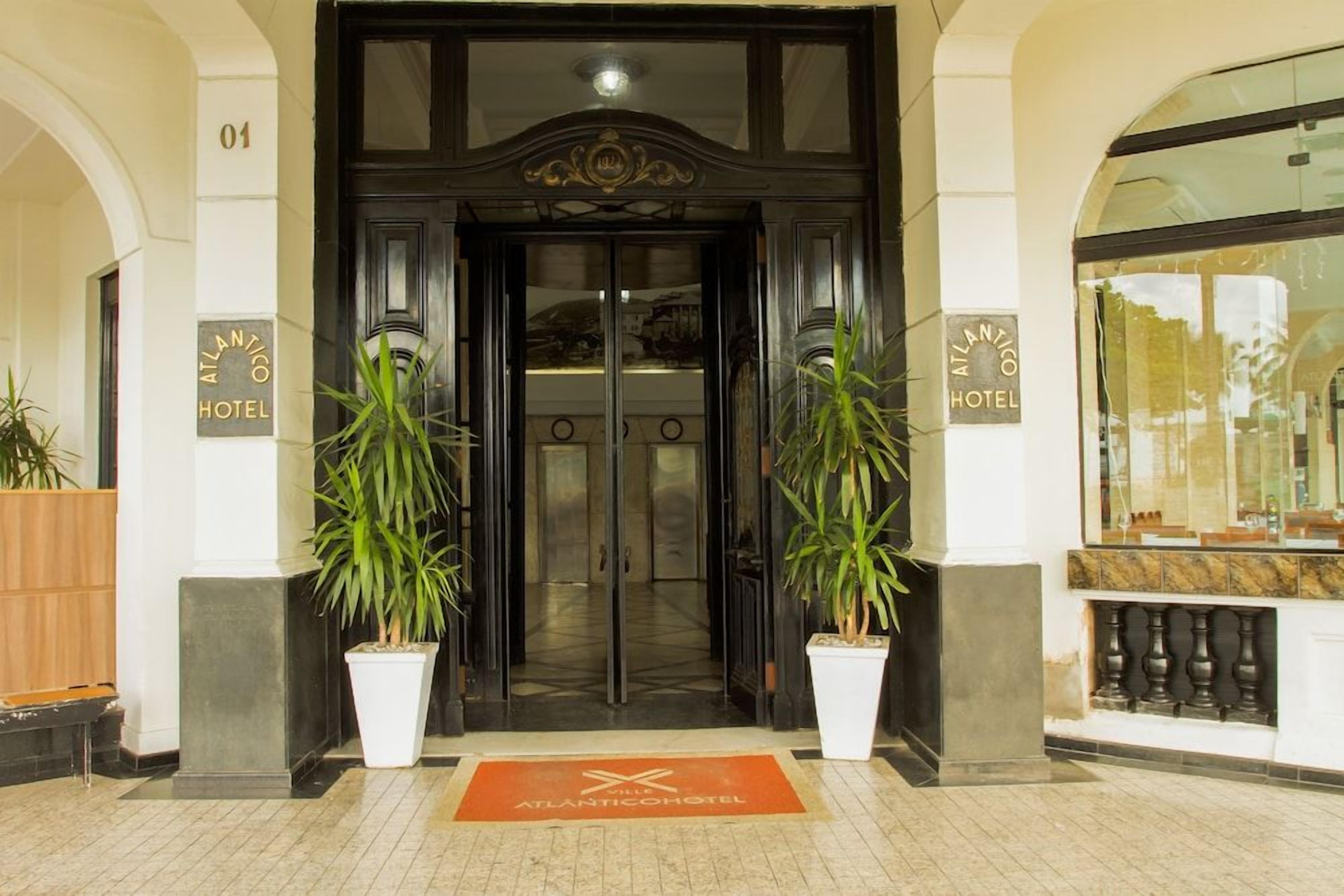 Entrada do Hotel Atlantic com porta dupla, plantas em vasos e tapete de entrada.