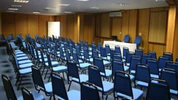 Uma sala de conferências com fileiras de cadeiras azuis e uma mesa branca à frente.