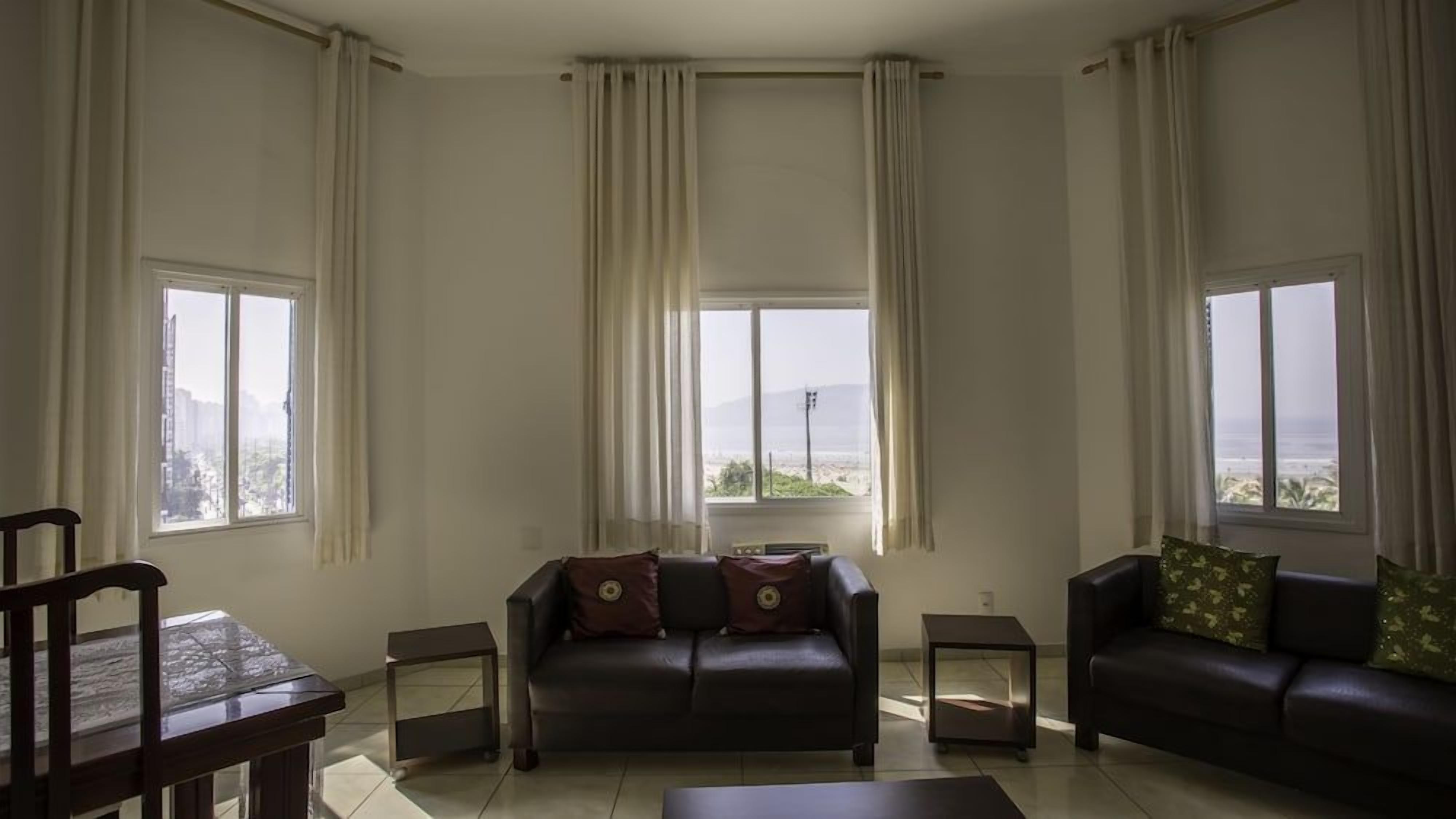 Uma sala de estar com sofá, mesa de centro, mesa de jantar e duas janelas com cortinas.