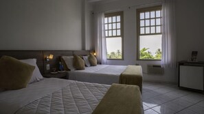 A hotel room with two beds, a nightstand, a small table, and a window with curtains.