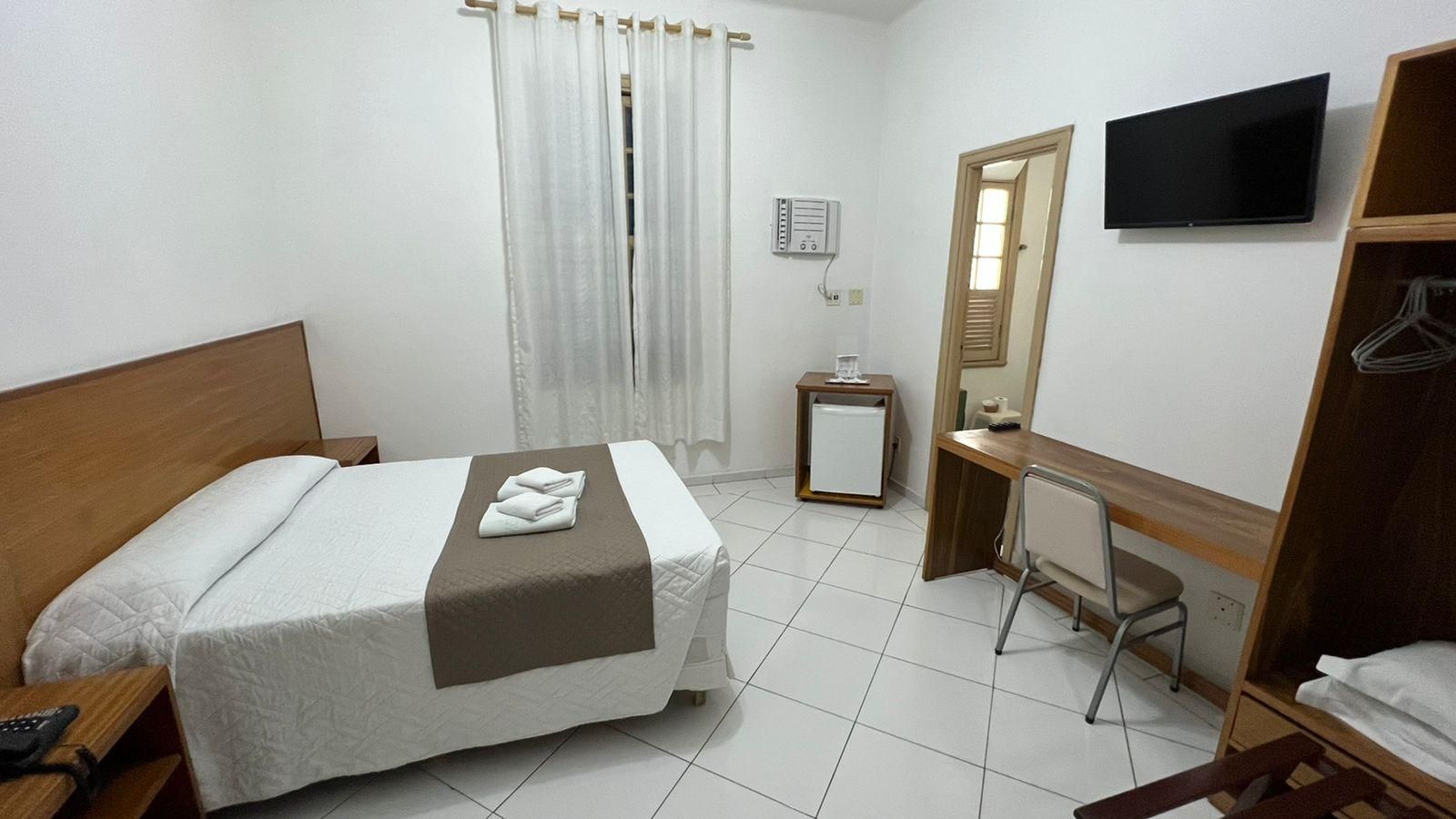 A hotel room with a bed, a desk, a chair, a TV, and a wardrobe.