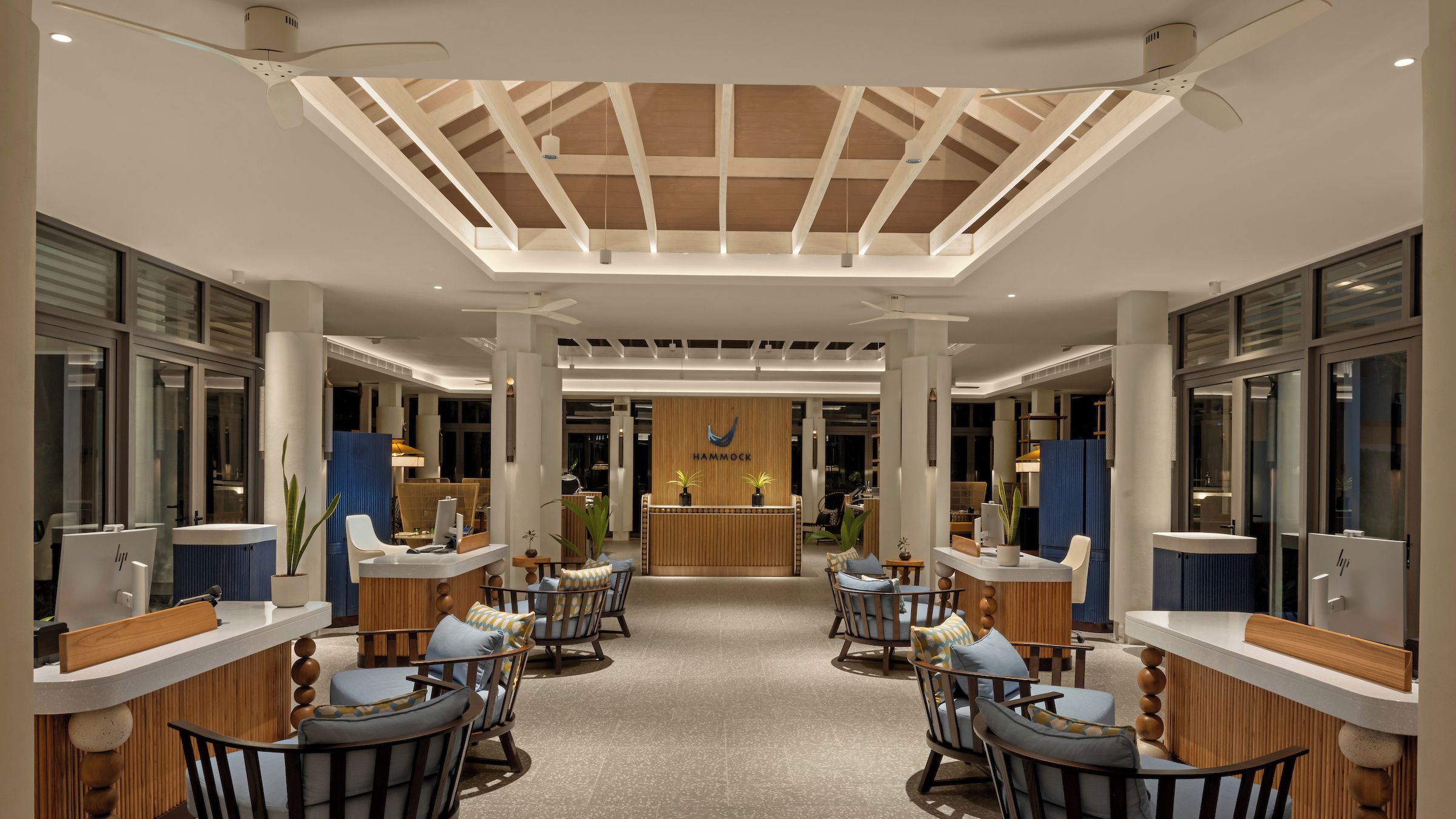 A hotel lobby with a central reception desk, seating area with chairs, and a skylight ceiling.