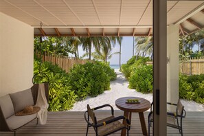 A covered outdoor area with a wooden deck, a sofa, and a table with a plate of fruit. - Avani+ Fares Maldives Resort (Fares)
