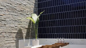 Une salle de bain moderne avec un mur en pierre, un mur recouvert de carreaux noirs, une baignoire, des étagères en bois et une plante en pot.