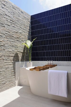 Une salle de bain moderne avec un mur en pierre, un mur recouvert de carreaux noirs, une baignoire, des étagères en bois et une plante en pot.