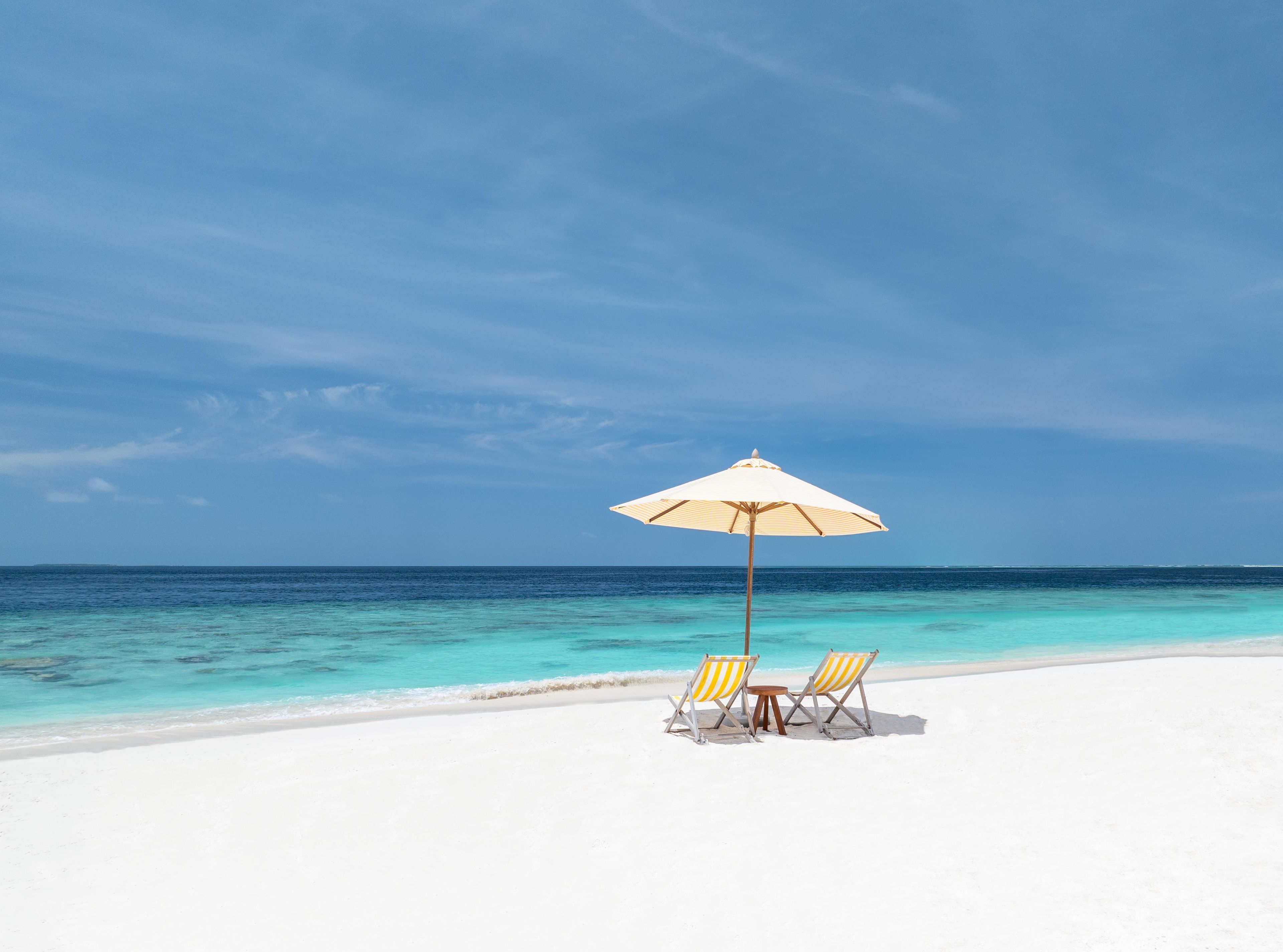 Una playa de arena blanca, mar azul transparente y una sombrilla.