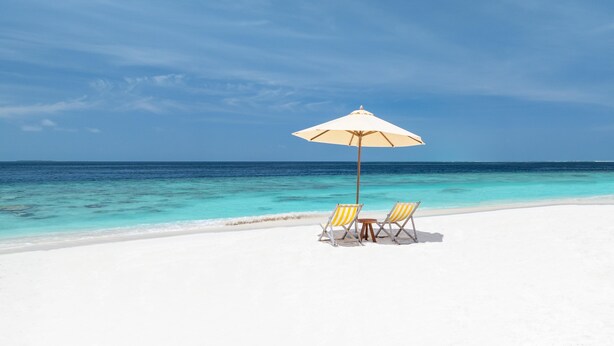 Une plage de sable blanc, une mer d’un bleu limpide et un parasol de plage.
