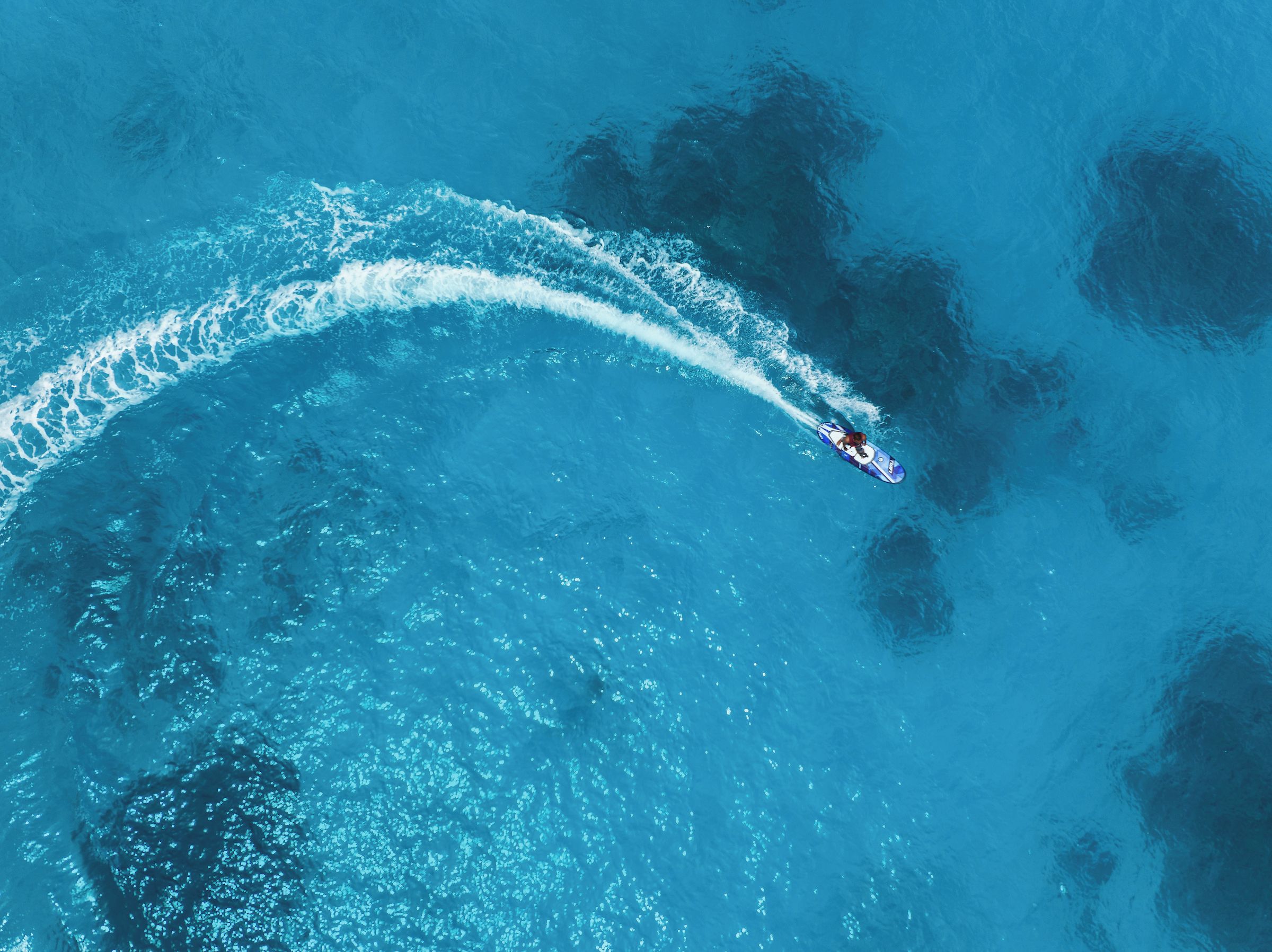 An aerial view of a boat creating a wake in a large body of water.
