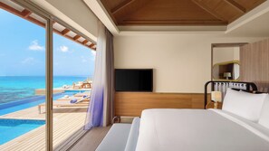 A hotel room with a large bed, a TV, a wooden headboard, a bedside table, and a view of the ocean and pool. - Avani+ Fares Maldives Resort (Fares)