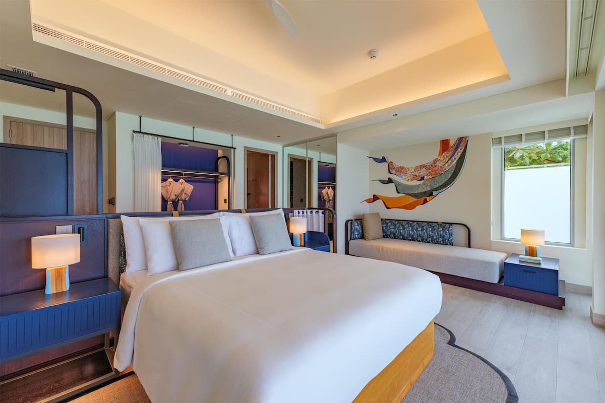 A modern hotel room with a large bed, a seating area, a wall-mounted TV, and a window with a view.